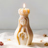 A white silicone mold shaped like a praying girl with hands clasped, holding a lit candle.