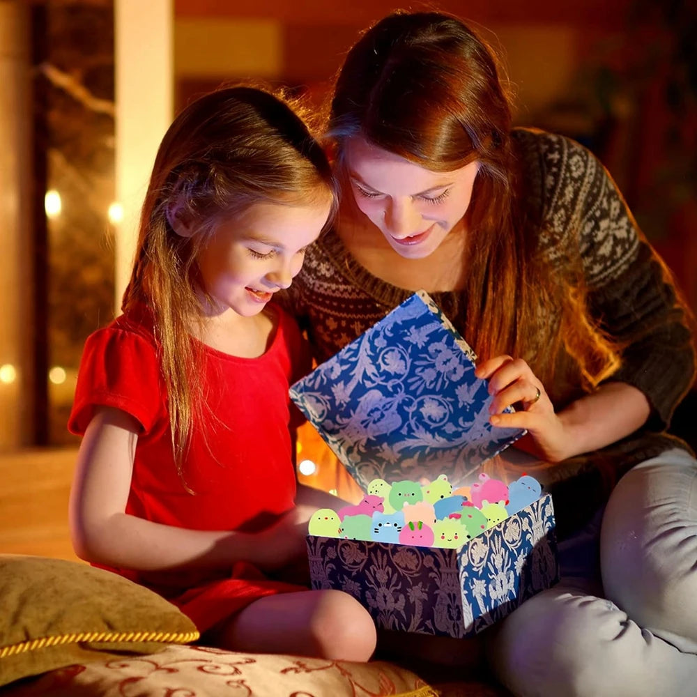 A woman and a girl are playing with colorful glow-in-the-dark animal squishies in a box.