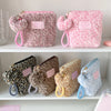 A collection of pink and leopard print cosmetic bags with fuzzy pom-pom charms displayed on a white shelf.
