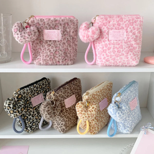 A collection of pink and leopard print cosmetic bags with fuzzy pom-pom charms displayed on a white shelf.