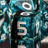 A close-up of a translucent blue resin die with the number 5, reflecting on a dark surface.