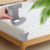 A hand is holding a gray invisible bedsheet corner tightener clip, demonstrating its use on a white quilted mattress.