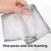 A hand is squeezing a gray, mesh cleaning cloth that is producing rich white foam.