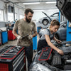 A man and a woman working on a car engine in a garage, using magnetic tools.