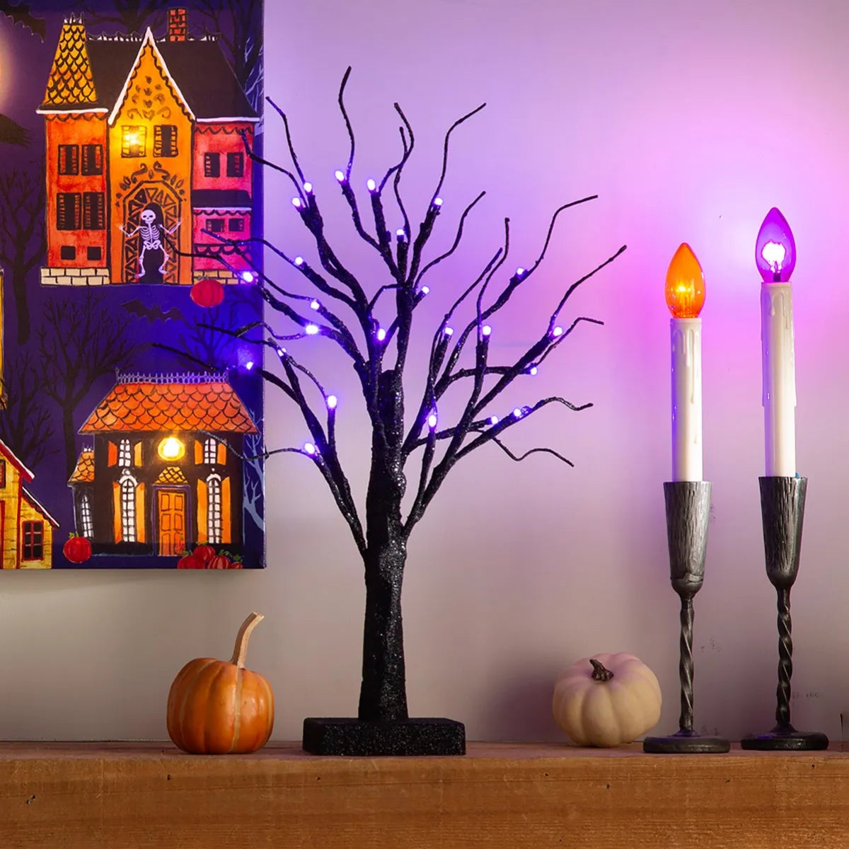 An LED Halloween birch tree with black branches illuminated by purple and orange lights sits on a wooden surface.