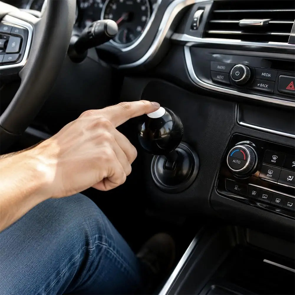 A hand is pressing a black push-to-start button cover with a billiard ball design on a car's interior dashboard.