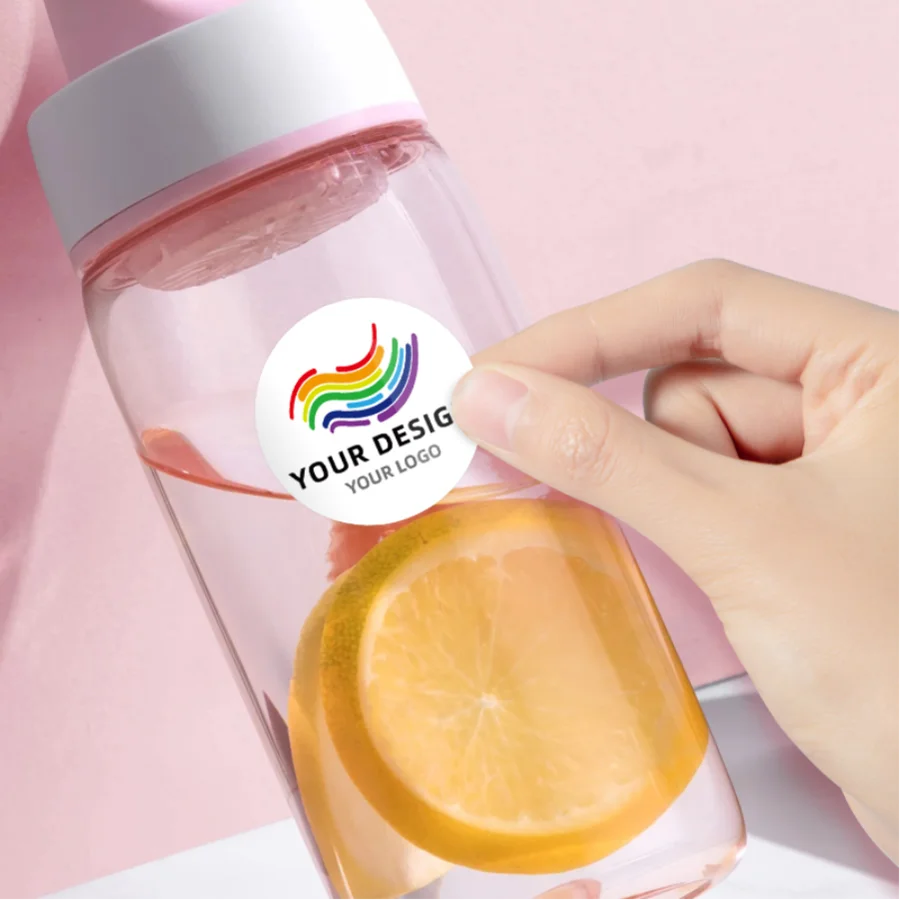 A hand holds a pink bottle with a custom label featuring a rainbow design and an orange slice.