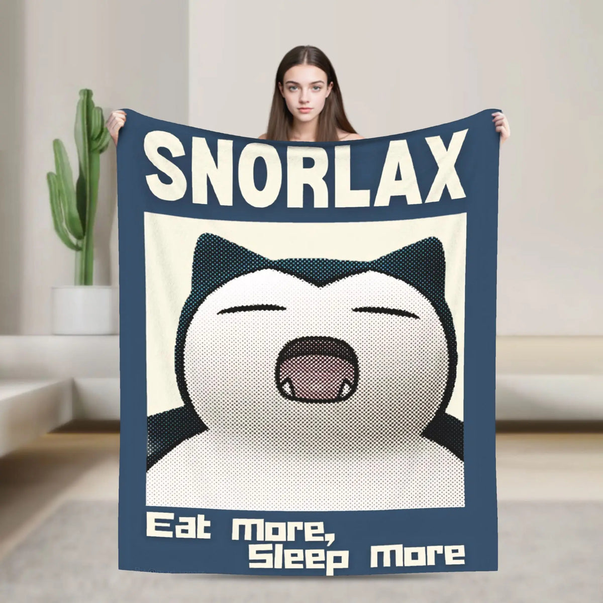 A person holds up a large dark blue blanket featuring a Snorelax face and the text Eat More Sleep More