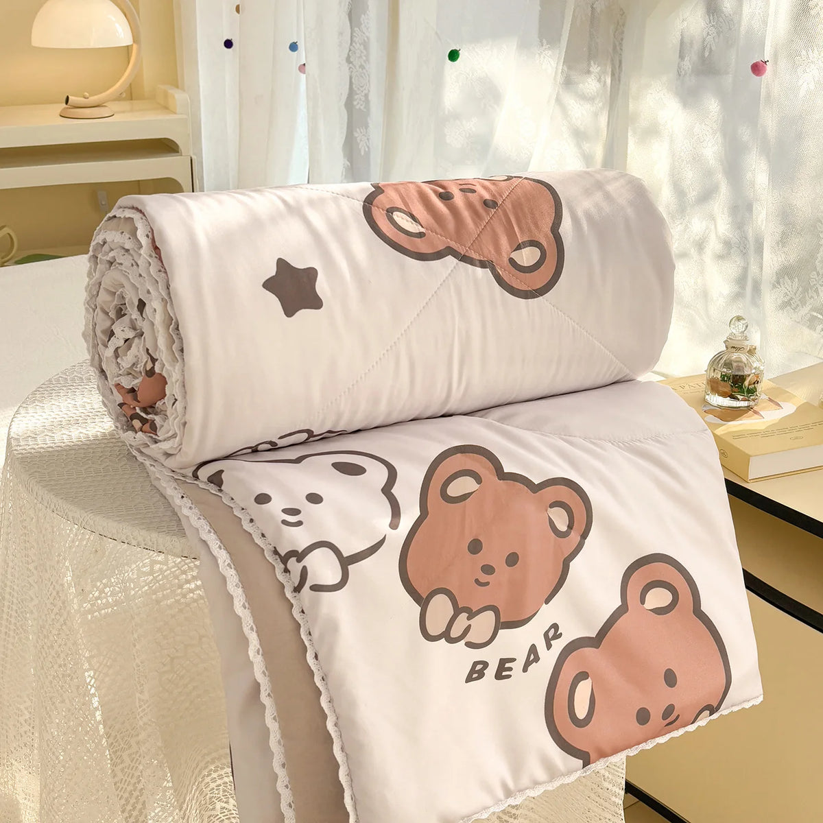 A rolled and unfolded panda print lightweight summer comforter with lace trim displayed on a white surface.