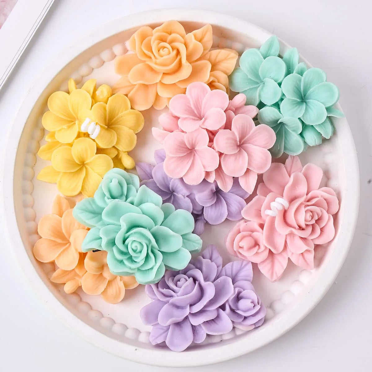 A collection of colorful frangipani gardenia flower silicone molds in shades of peach, yellow, mint green, and lavender.