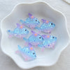 A collection of iridescent blue and purple resin charms shaped like fish are displayed in a white dish.