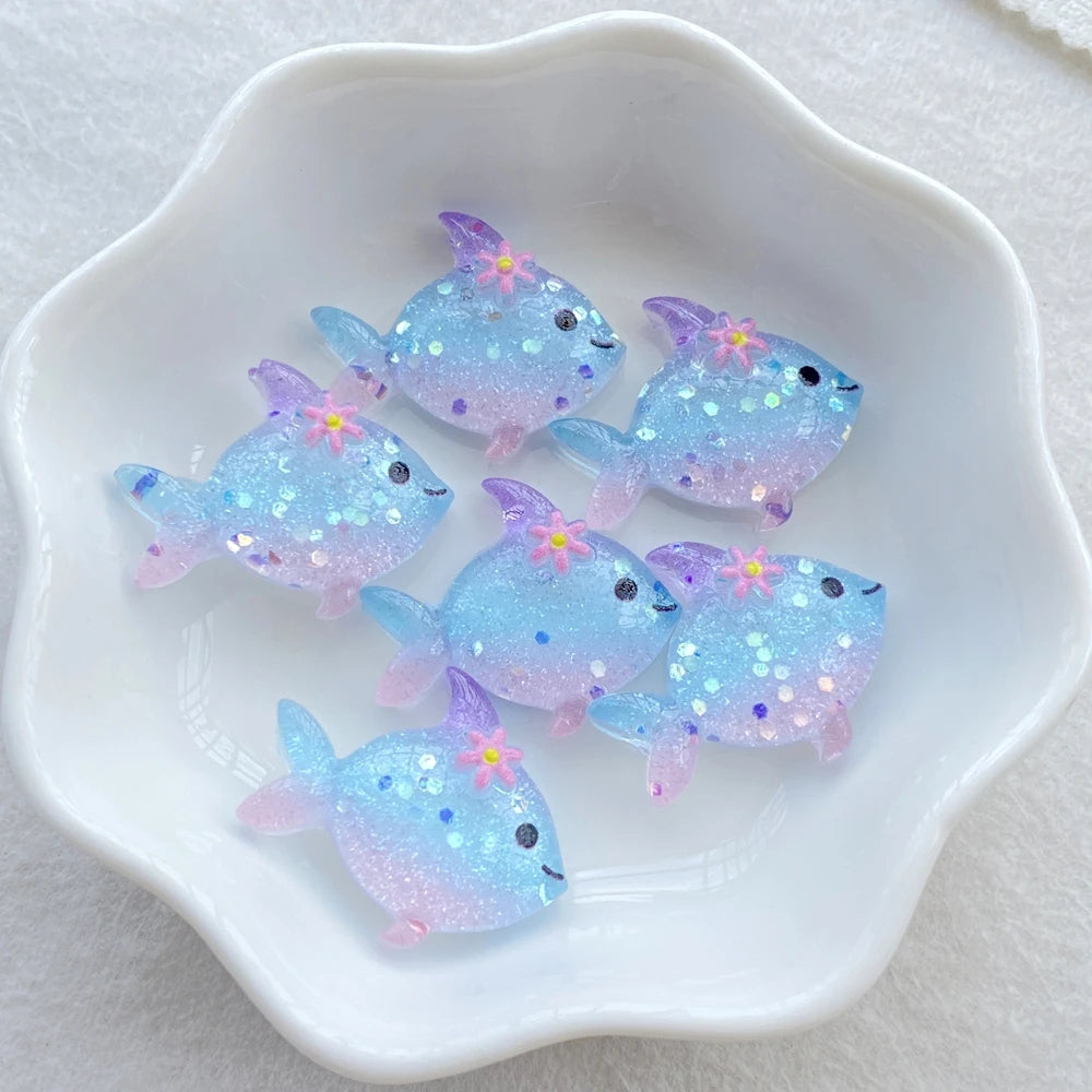 A collection of iridescent blue and purple resin charms shaped like fish are displayed in a white dish.