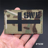 A rectangular camouflage patch featuring a black cross and the text SWE on a fabric background.