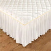 White quilted embroidered bed skirt with gold trim draped on a wooden floor.