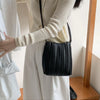A woman wearing a white dress holds an elegant black pleated faux leather crossbody bag.