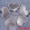 A set of five silver glitter heart iron-on embroidered patches placed on a blue denim fabric.