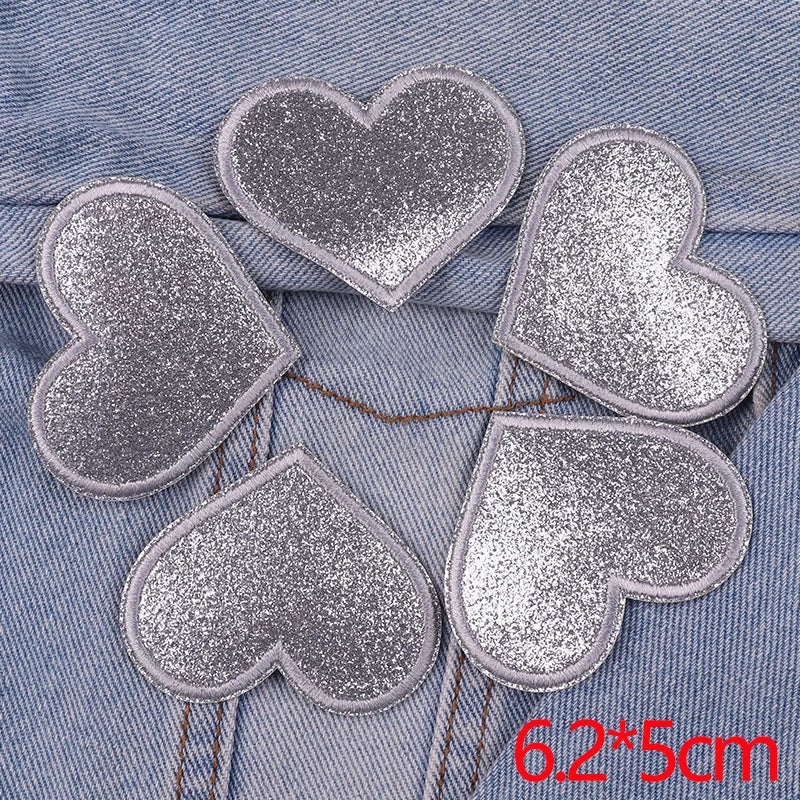 A set of five silver glitter heart iron-on embroidered patches placed on a blue denim fabric.