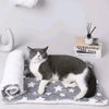 A gray and white cat is lying on a plush mat, with a rolled white towel nearby.