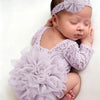 A newborn baby wearing a lavender lace romper with a ruffled tutu and a matching headband, lying down.