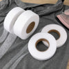 Rolls of white double-sided iron-on fabric adhesive tape lying on a gray cloth.