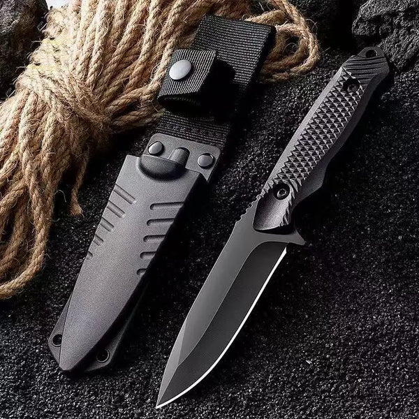 A black stainless steel fixed blade outdoor knife with a sheath resting on a dark surface next to thick rope.