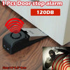 A black wireless door stop alarm device with a red signal, placed on a wooden floor next to a white cabinet.