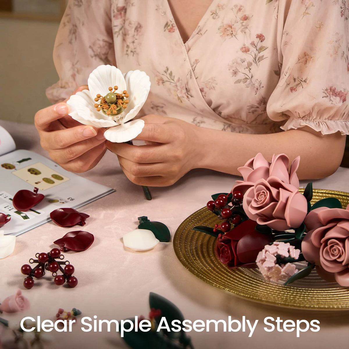 A person is assembling a pink rose bouquet set with various colored floral building blocks on a table.