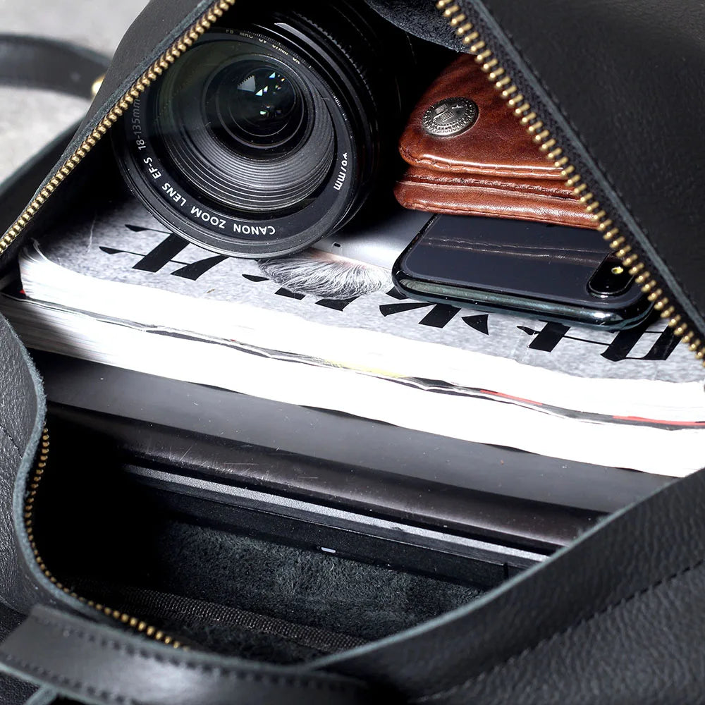 Nahaufnahme im schwarzen Lederrucksack mit Kameraobjektiv, Smartphone und Papier.