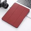 A red Retro Marble iPad Pro case with a built-in pencil holder is shown next to a silver laptop and camera.