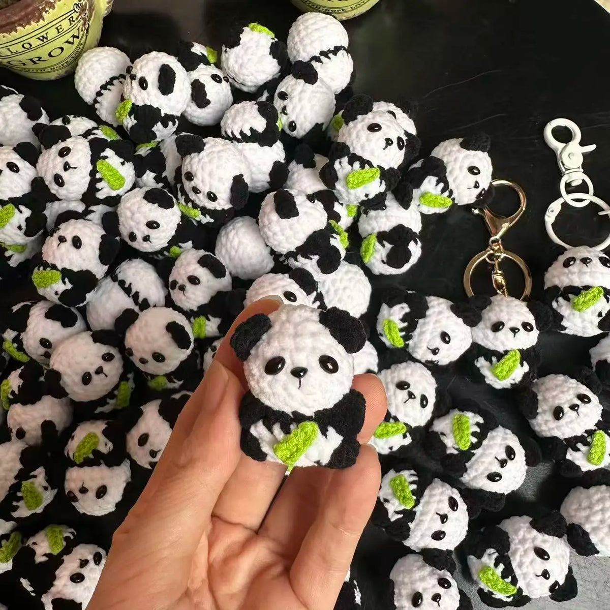 A hand holds a cluster of handmade crochet kitten keychains featuring cute panda and cartoon animal charms.