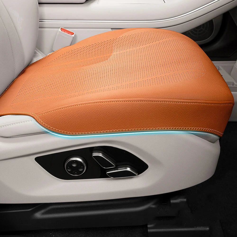 An orange breathable leather car seat cushion with a blue light accent is shown in a white vehicle interior.