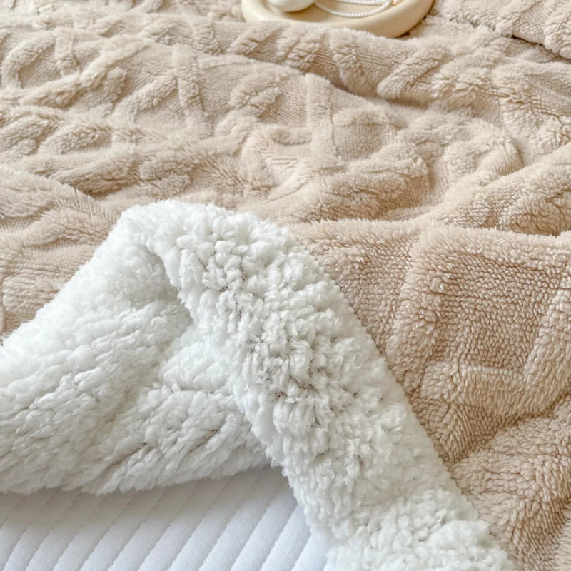 A white fluffy fleece throw blanket draped over a beige textured blanket.