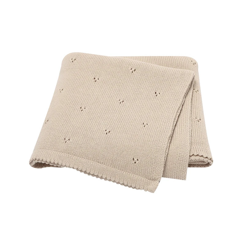A beige knitted soft cotton baby blanket with small eyelet details, folded for display.