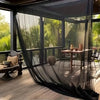 A black mesh netting is draped over a large glass window, obscuring a lush green garden view.
