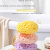 A stack of cheese bath balls in yellow, pink, and purple on a wooden surface.
