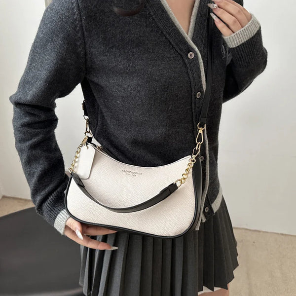 A woman is holding a white leather crossbody bag with gold hardware against a dark gray sweater and skirt.