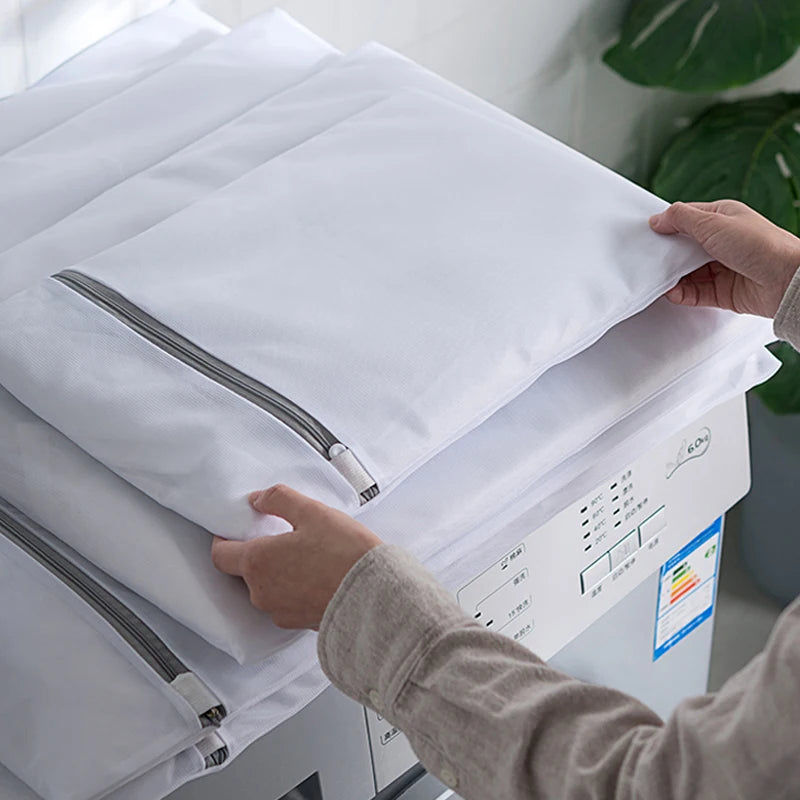 A hand is placing a white mesh laundry bag into a washing machine, demonstrating the delicates wash bags.