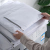 A hand is placing a white mesh laundry bag into a washing machine, demonstrating the delicates wash bags.