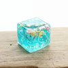 A clear blue ice cube shaped stress relief squeeze toy filled with glitter and sea creatures.