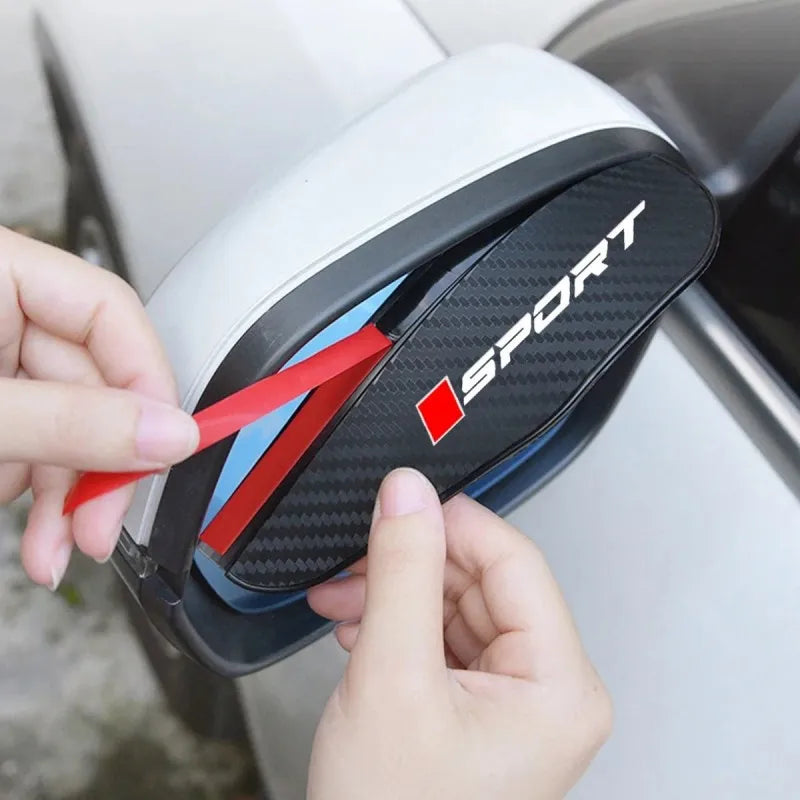 A hand is holding a black carbon fiber rain cover for a car side mirror, showing the SPORT logo.