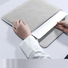 A hand is placing a white laptop into a gray slim sleeve case, demonstrating a hidden magnetic bracket feature.