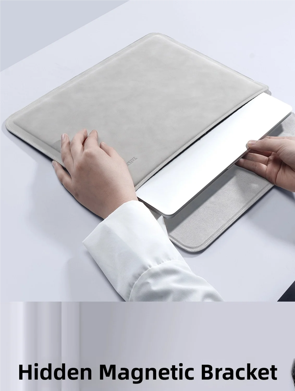 A hand is placing a white laptop into a gray slim sleeve case, demonstrating a hidden magnetic bracket feature.
