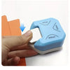 A hand holds a light blue corner cutter tool with various angle options, demonstrating its use for cutting paper and cards.