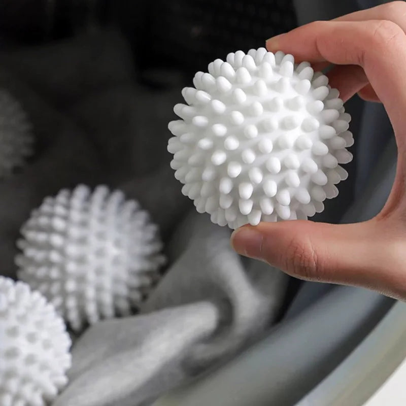 A hand holds a white reusable laundry ball with a textured surface, placed in a gray fabric container.