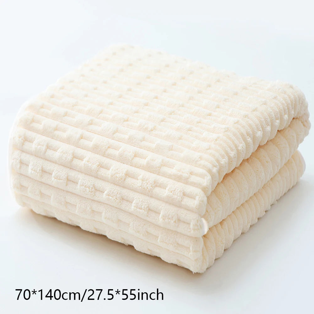 A stack of soft, beige coral velvet bath towels folded neatly on a white surface.