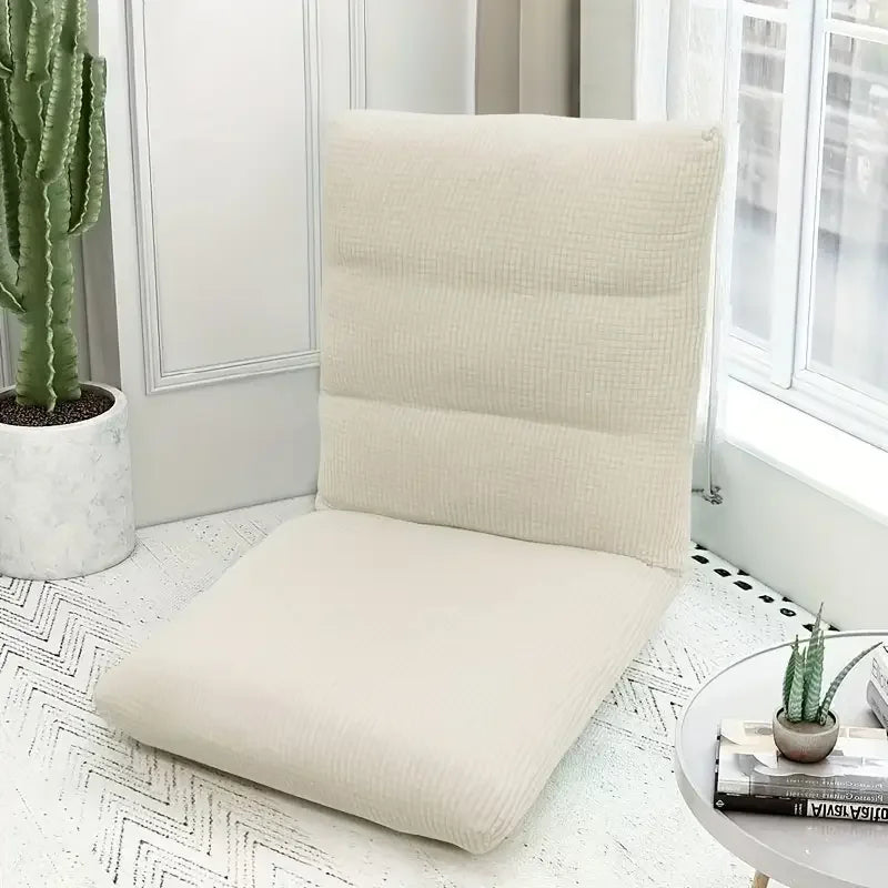A beige foldable floor sofa cover for a single seat is displayed on a white rug next to a potted cactus.