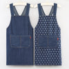 A pair of navy blue striped denim cross-back aprons displayed on a hanger.