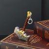 A detailed metal sword keychain featuring a brown grip and gold accents rests on a leather-bound book.