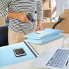 A person is preparing blue bubble mailers for shipping on a desk next to a laptop.
