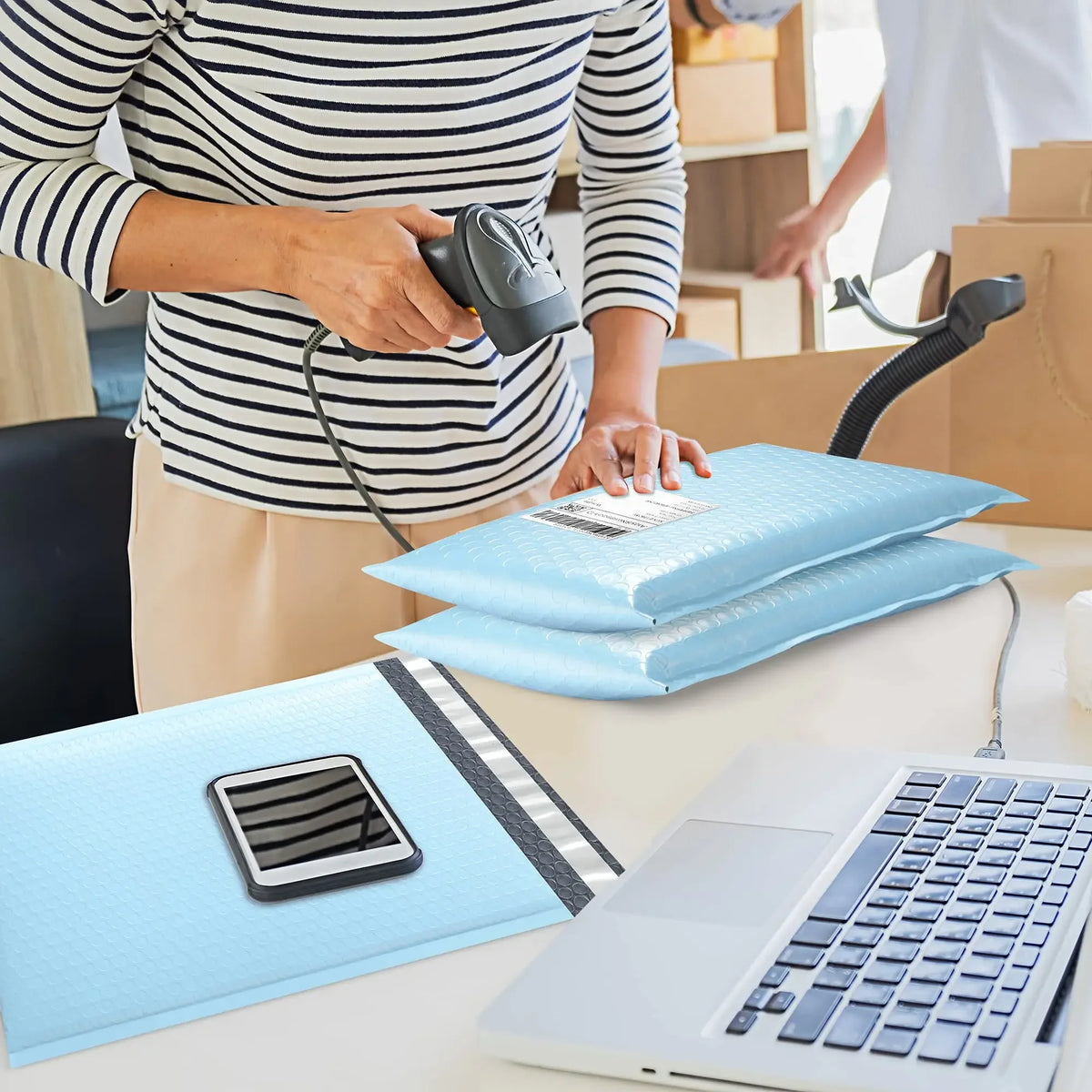 A person is preparing blue bubble mailers for shipping on a desk next to a laptop.